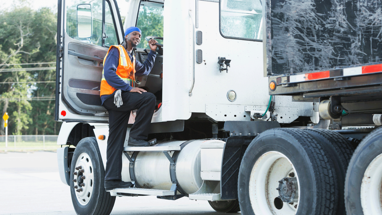 Truck driver, wearing an orange safety vest, exiting a semi-truck.