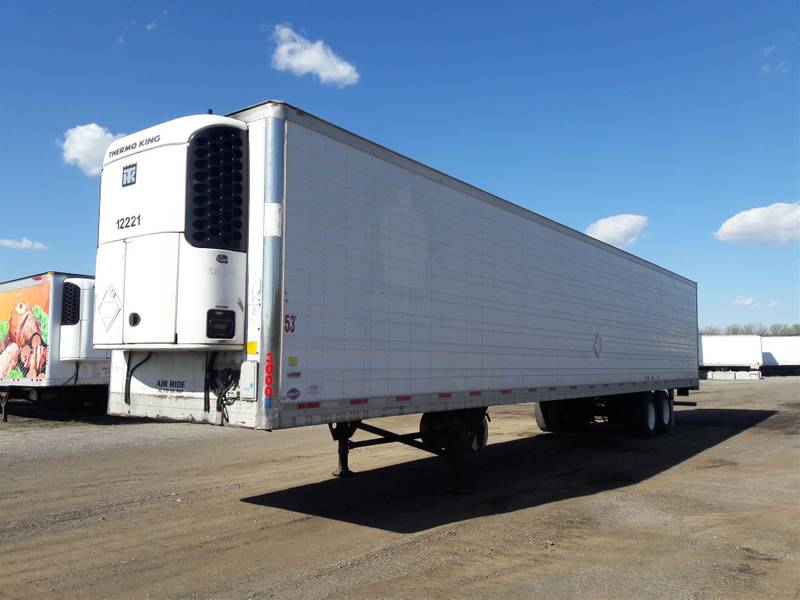 A white refrigerated trailer is parked in a parking lot
