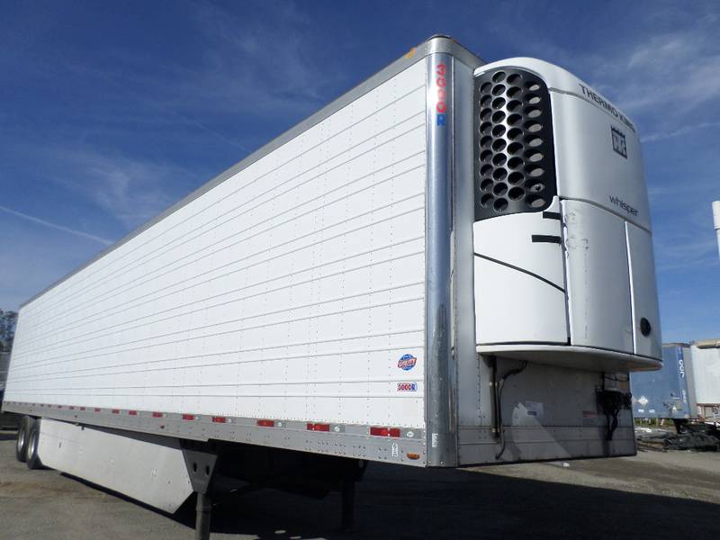 A white refrigerated trailer is parked in a parking lot.