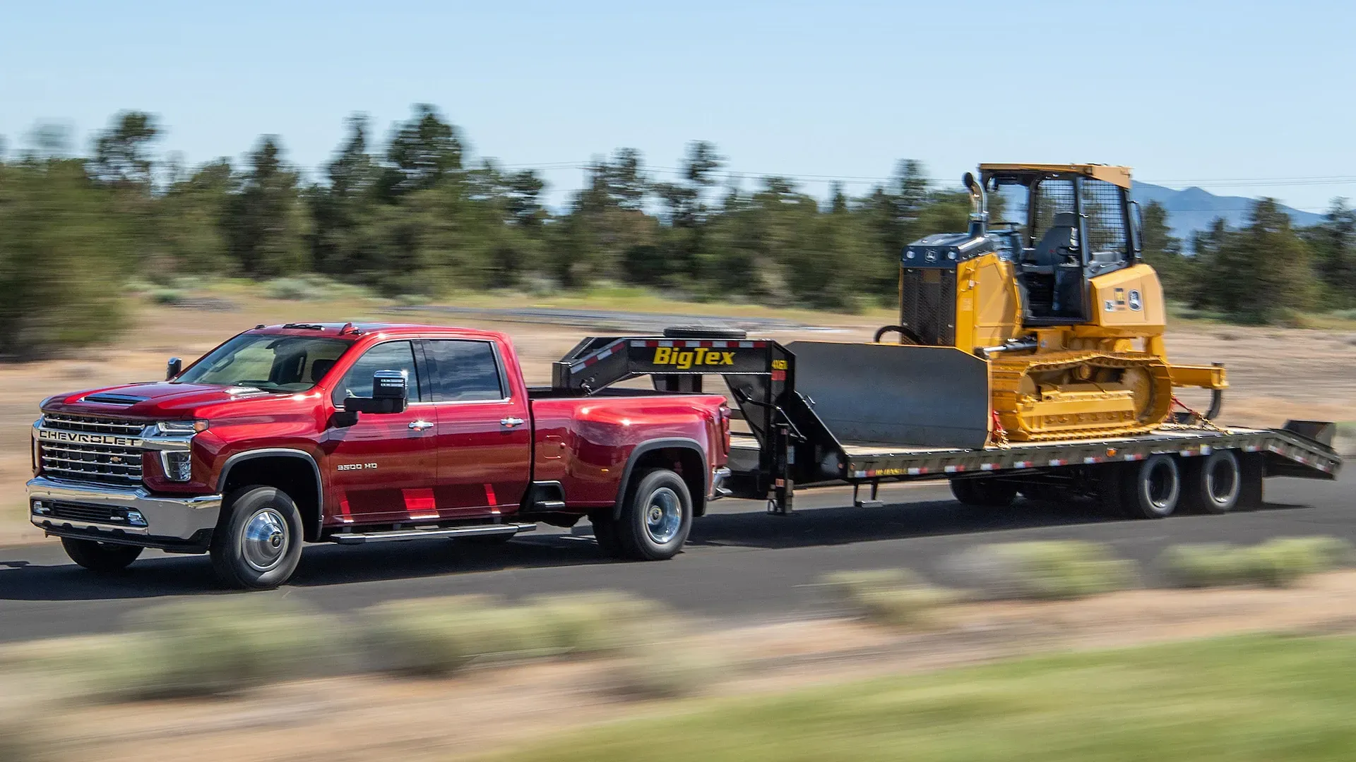 A red truck is towing a yellow bulldozer on a trailer.