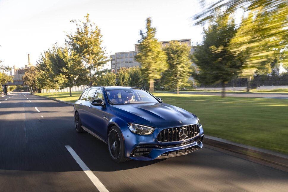 A blue mercedes benz e63 amg is driving down a street next to a park.