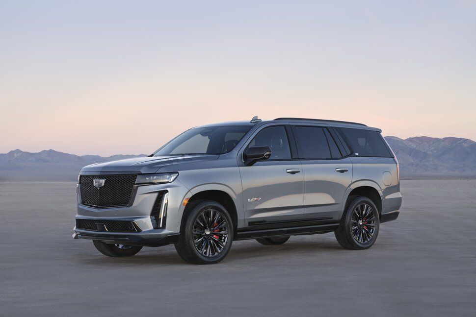 A silver cadillac escalade is parked in the middle of a desert.