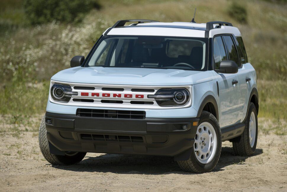 A white ford bronco sport is parked in a dirt field.