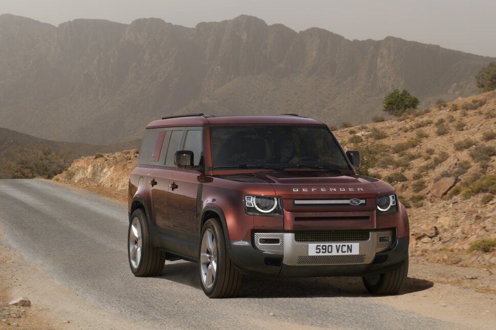 A red land rover defender is driving down a dirt road.