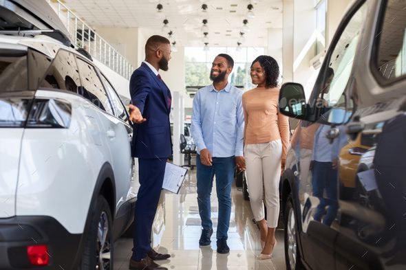 A man is talking to a couple in a car showroom.
