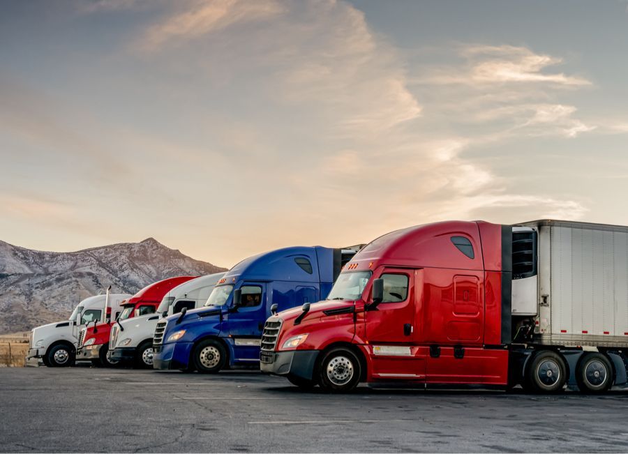 Line of colorful semi-trucks parked on asphalt, mountains in the background, dusk.