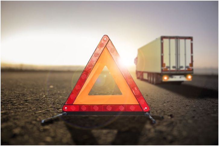 A warning triangle is sitting on the side of the road next to a truck.