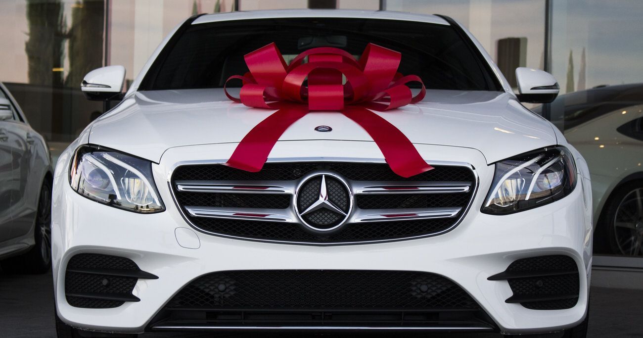 A white mercedes benz with a red bow on the hood.