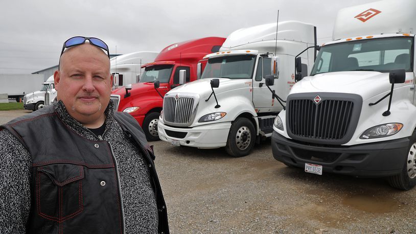 A man is standing in front of a row of semi trucks.
