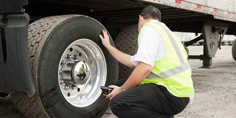 A man in a yellow vest is checking the tire of a semi truck.