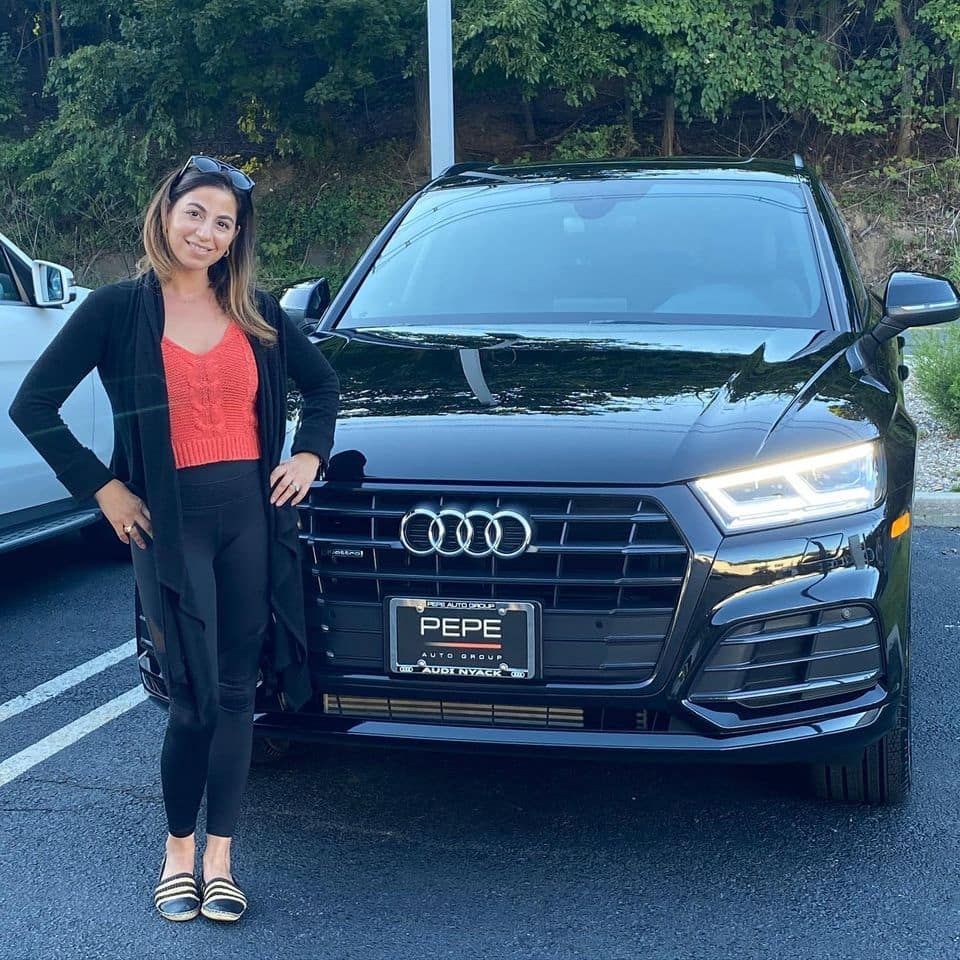 A woman is standing in front of a black audi car.