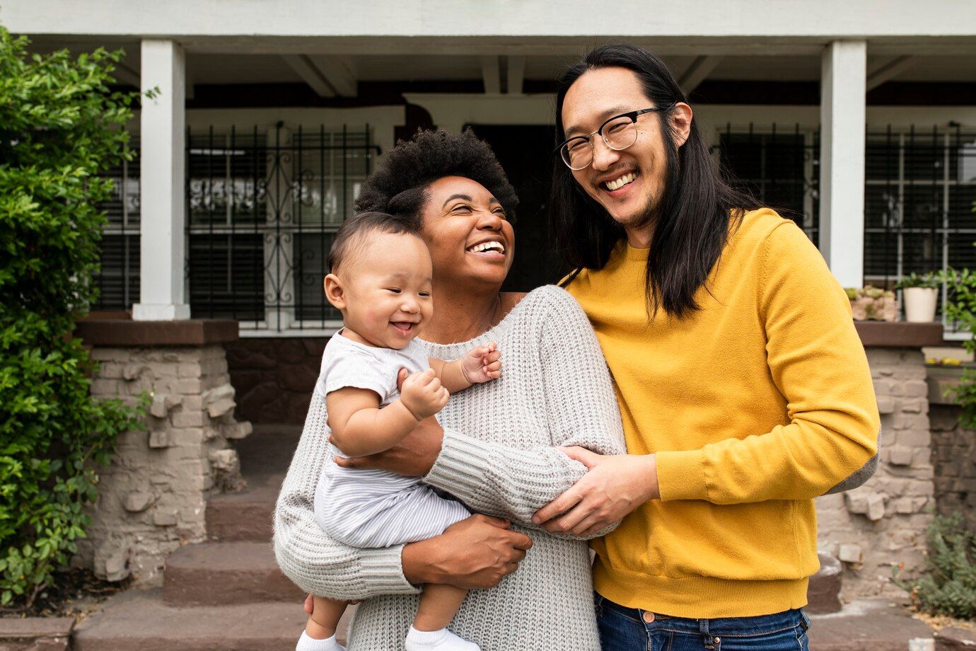 A man and woman are holding a baby in front of a house.
