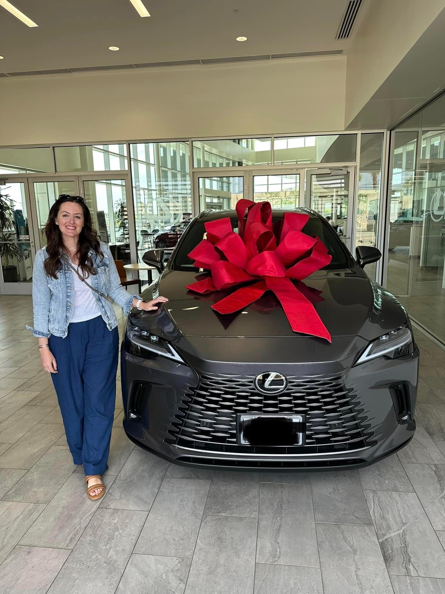 A woman is standing in front of a car with a red bow on it.