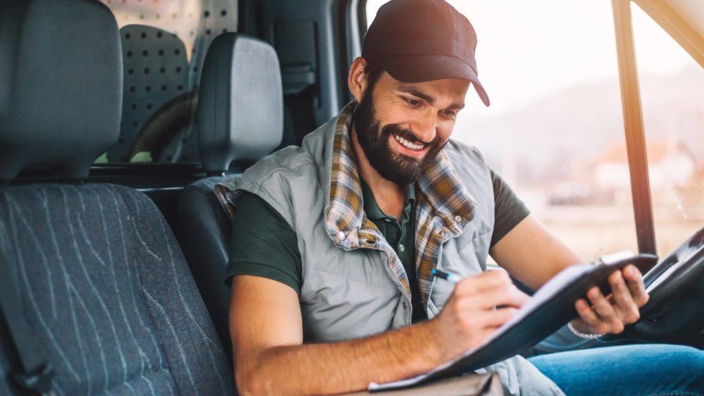 A man is sitting in the back seat of a truck reading a book.