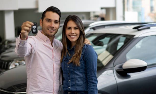 A man and a woman are holding a car key in front of a car.