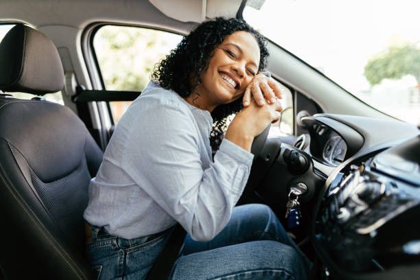 A woman is sitting in the driver 's seat of a car talking on a cell phone.