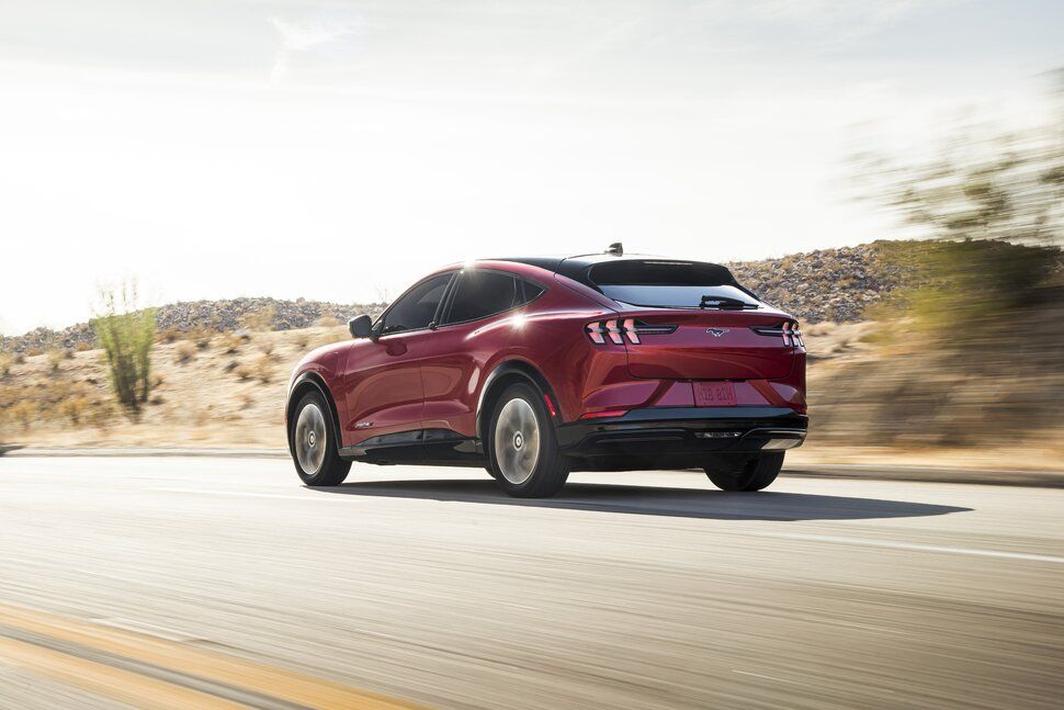 A red ford mustang mach e is driving down a desert road.