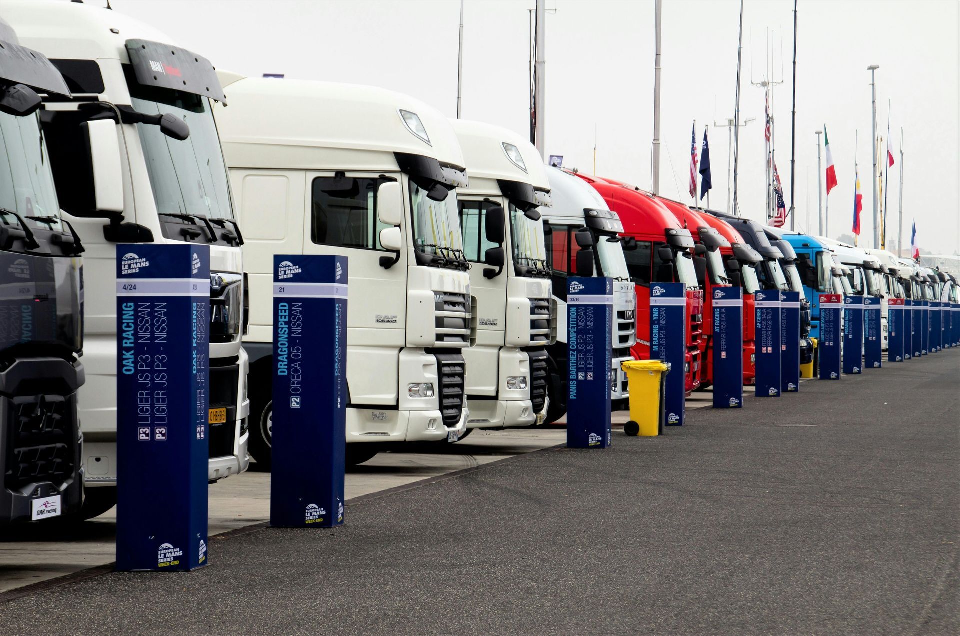 Trucks parked in a row next to blue charging stations. Flags are in the background.
