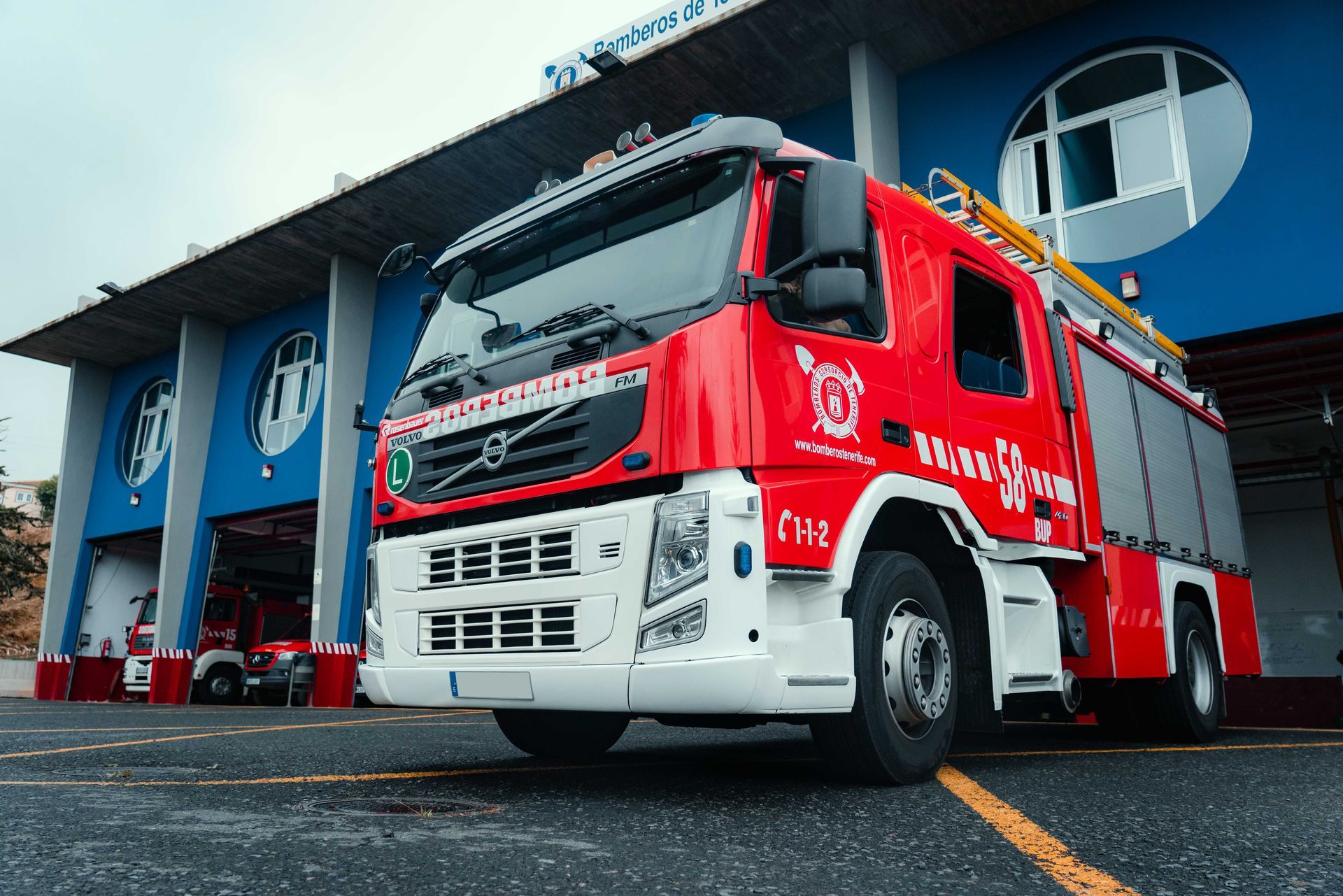 Red fire truck parked outside a blue fire station, viewed from a low angle.