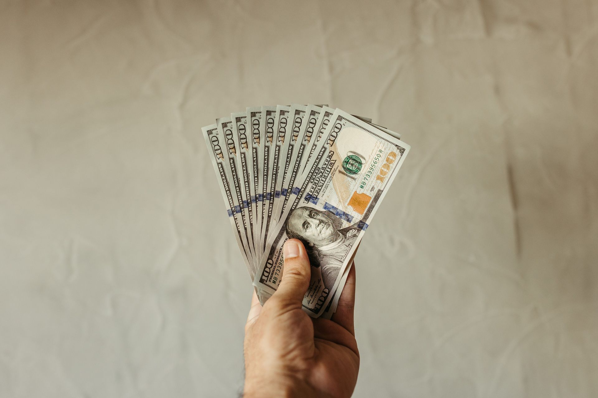 Hand holding a fan of banknotes against a plain beige background