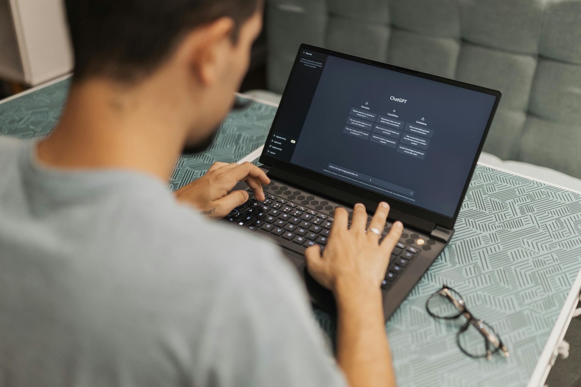 A person typing on a laptop screen displaying a diagram, with glasses resting on a patterned table.
