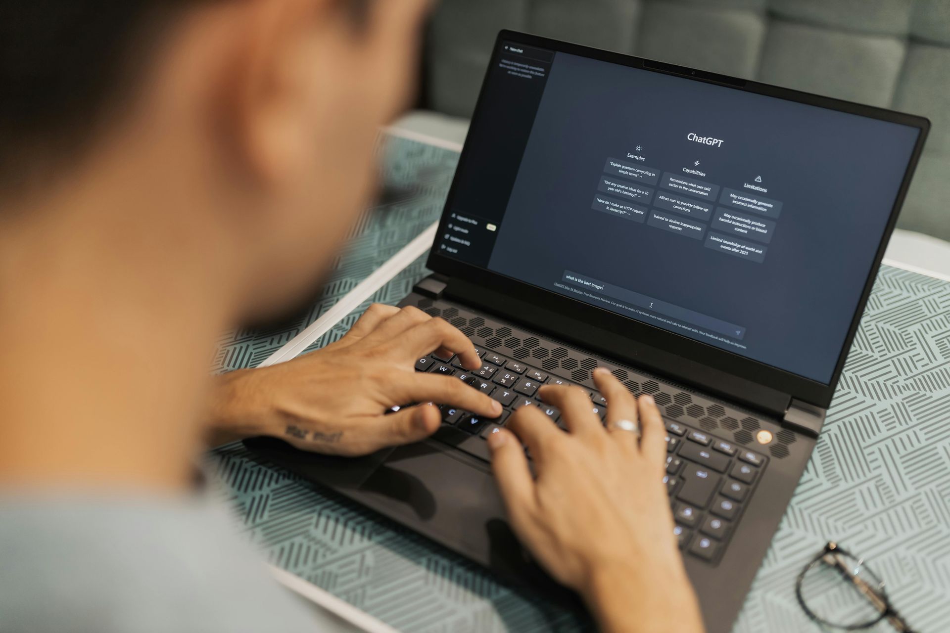 Person typing on a laptop with a dark screen showing code, viewed from over the shoulder.