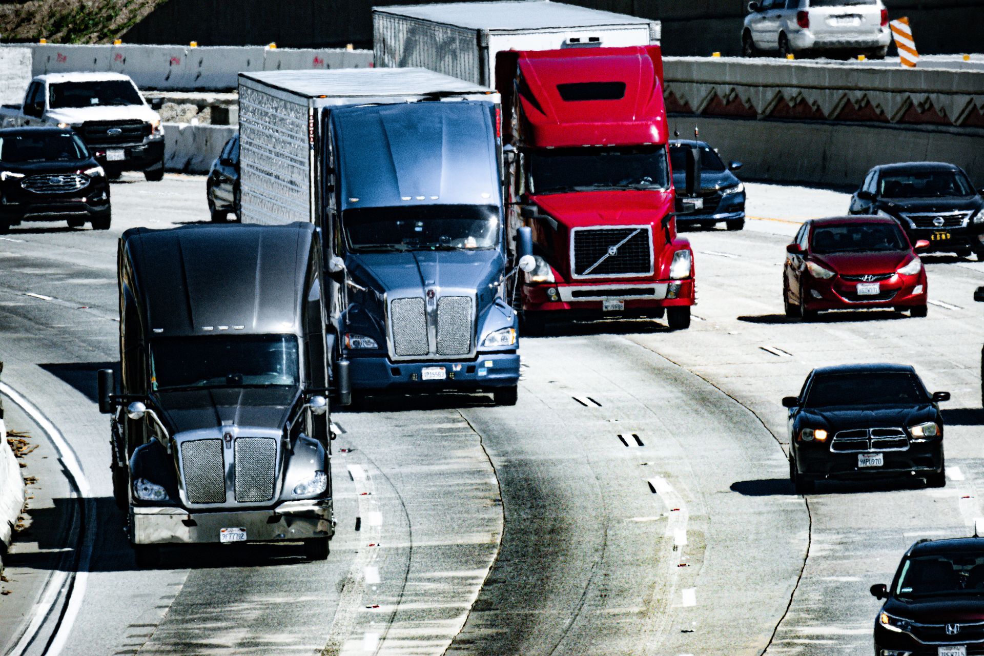Semi-trucks and cars traveling on a busy multi-lane highway in daylight.