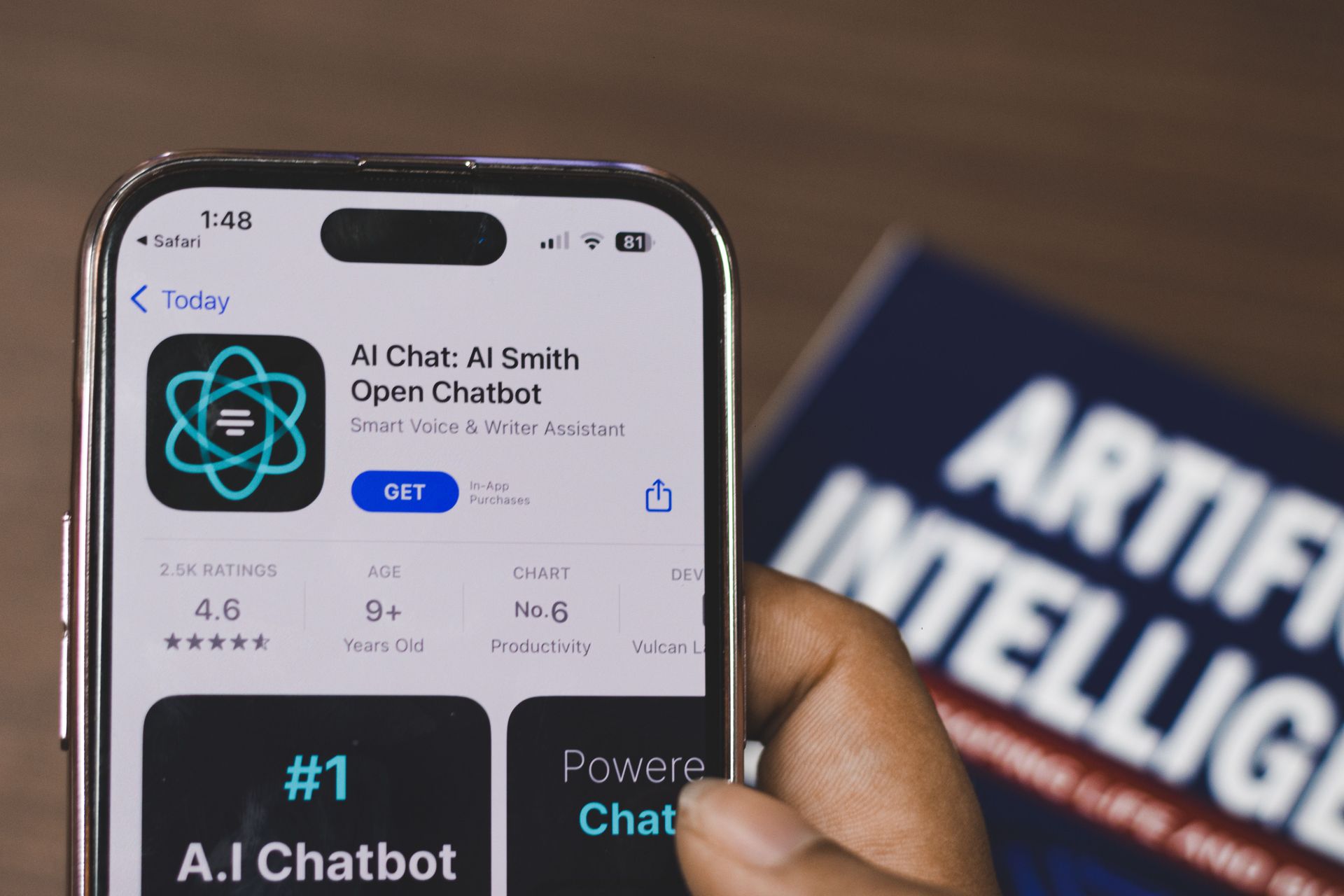 Hand holding a phone showing the AI Chat Smith app, with blurred “ARTIFICIAL INTELLIGENCE” text in background