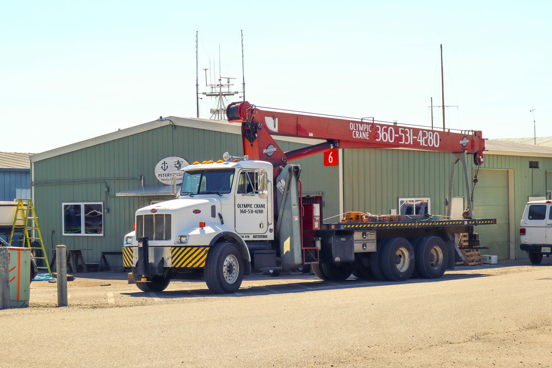 White crane truck parked outside a green building on a sunny day.