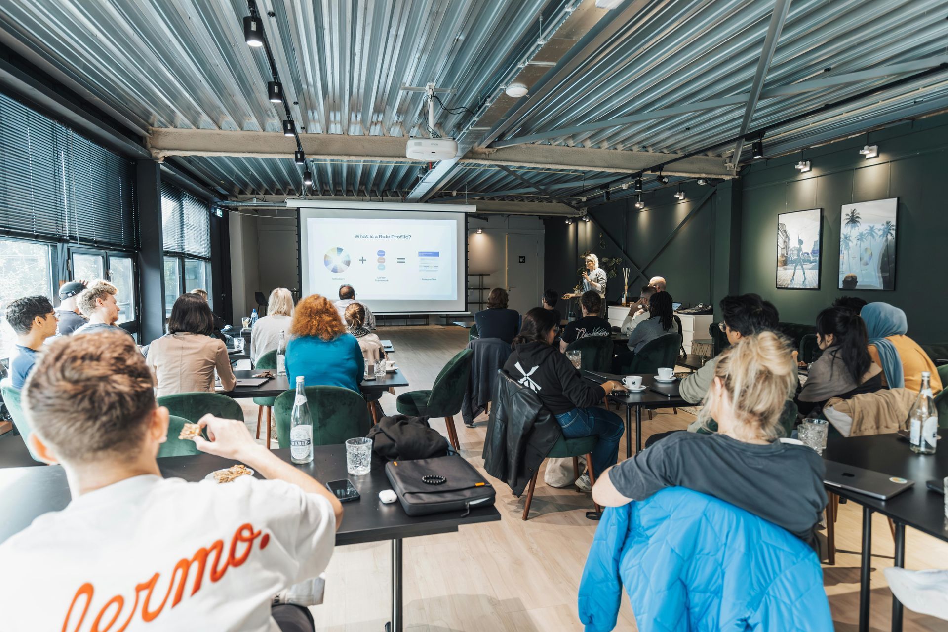 A group of people attending a seminar in an office space with a projector screen at the front.
