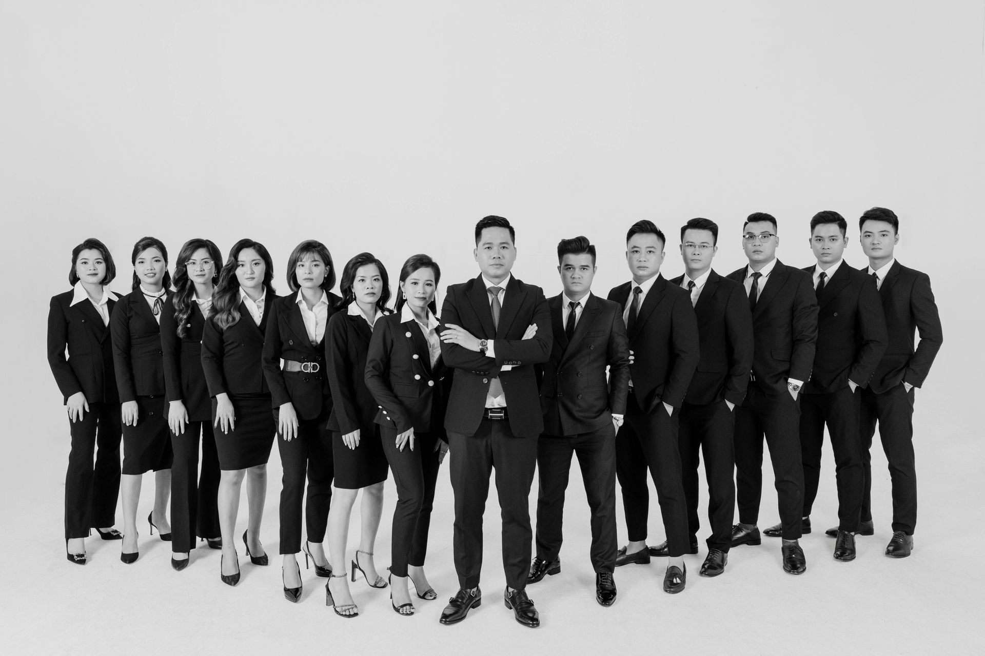 Group of people in matching dark suits posing in a studio against a white background.