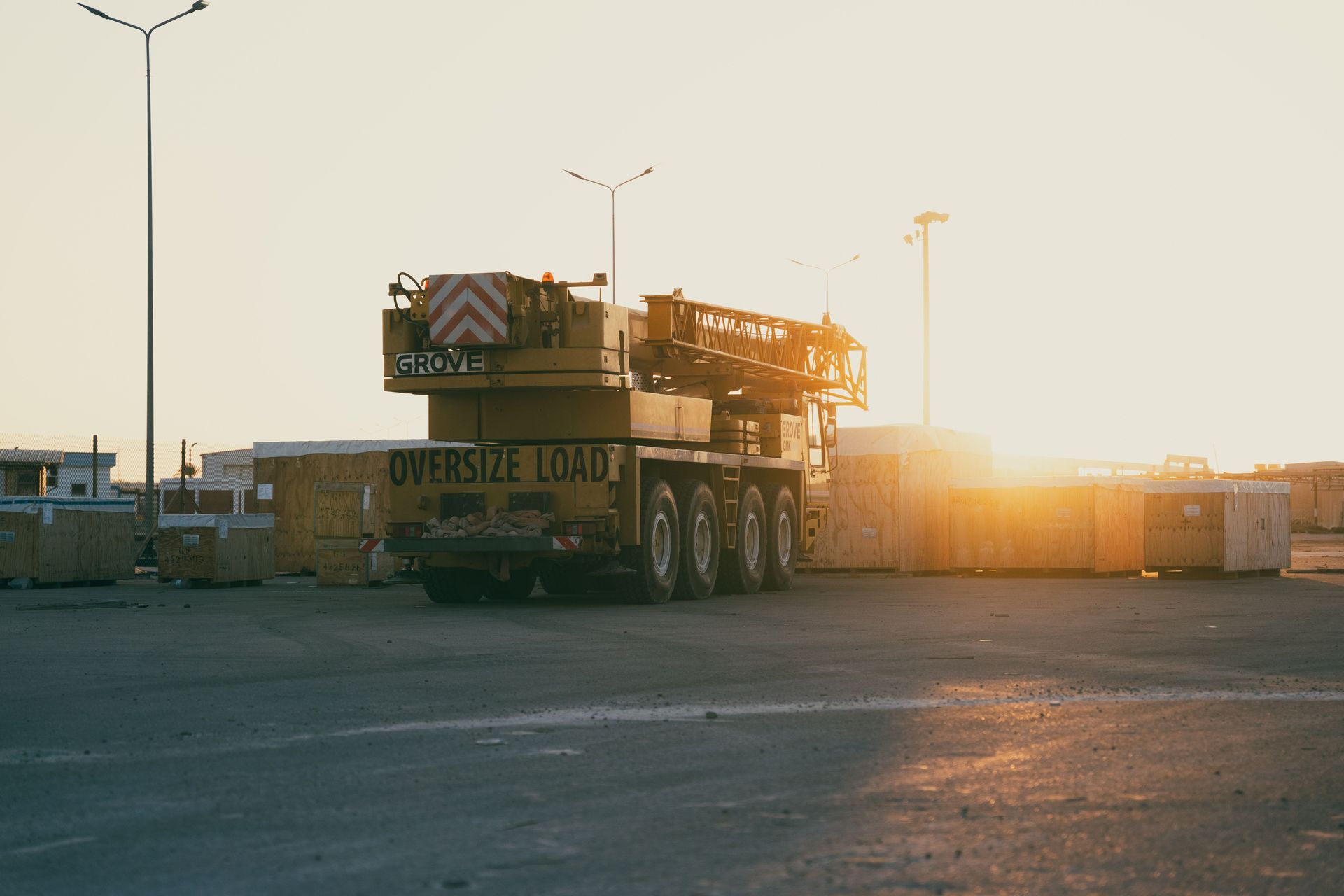 Flatbed truck carrying a large machine in a sunlit industrial lot at sunset