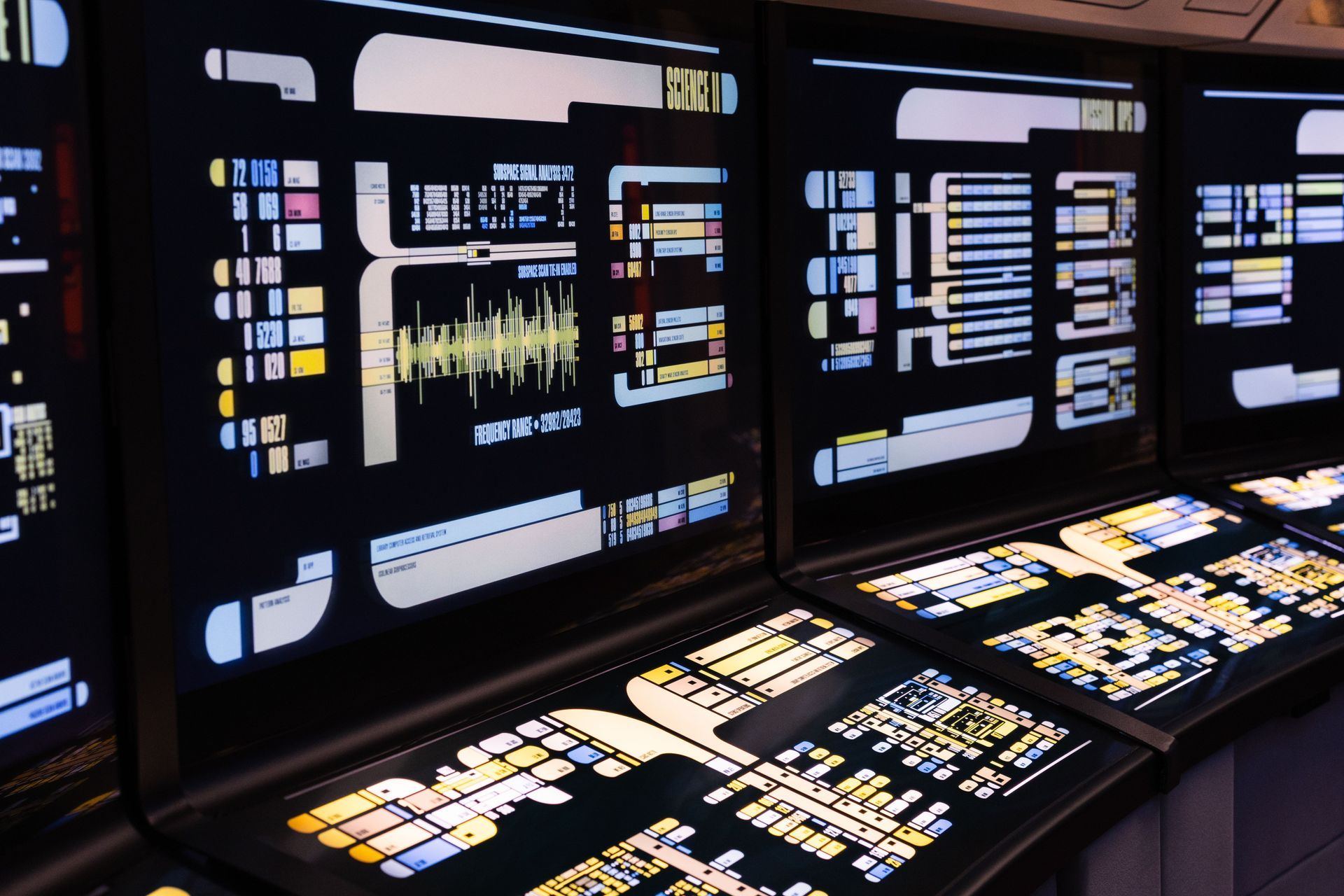 Futuristic control room with glowing monitors and panels displaying colorful data and schematics