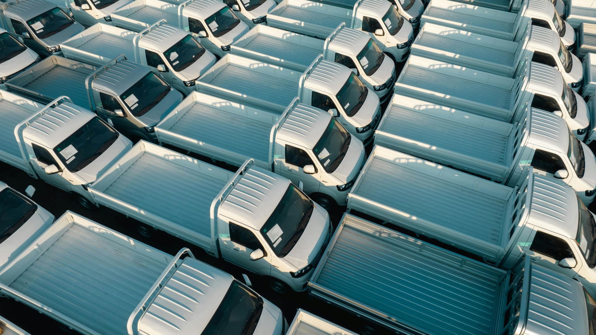 An aerial view of many identical white pickup trucks parked in neat rows in a lot.