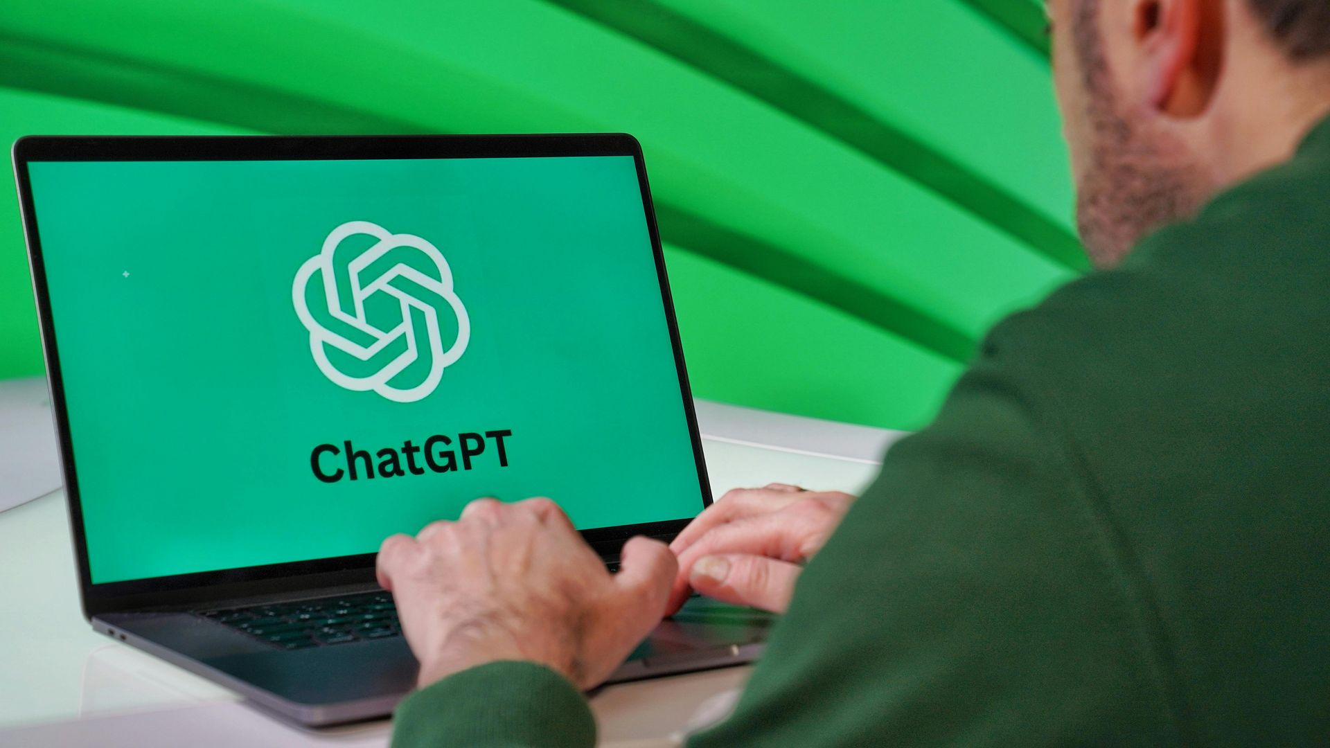 A person typing on a laptop displaying the ChatGPT logo against a vibrant green background.