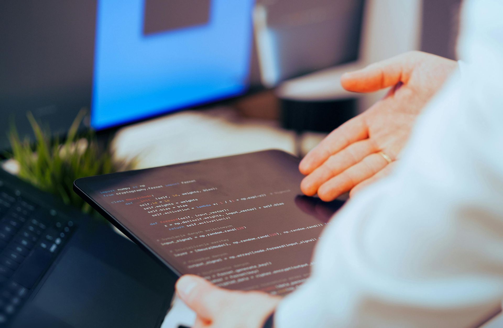Hands reaching over a laptop showing code on a dark screen in a bright office setting