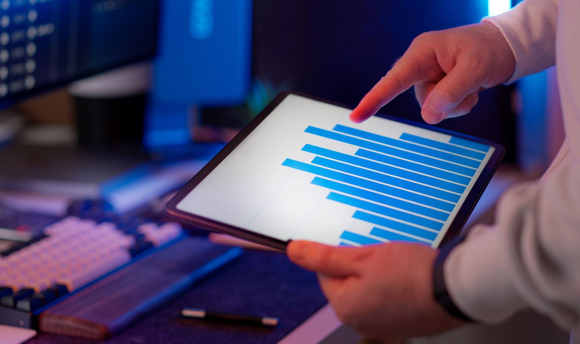 Hands using a tablet with blue bar charts on a desk in a dim office