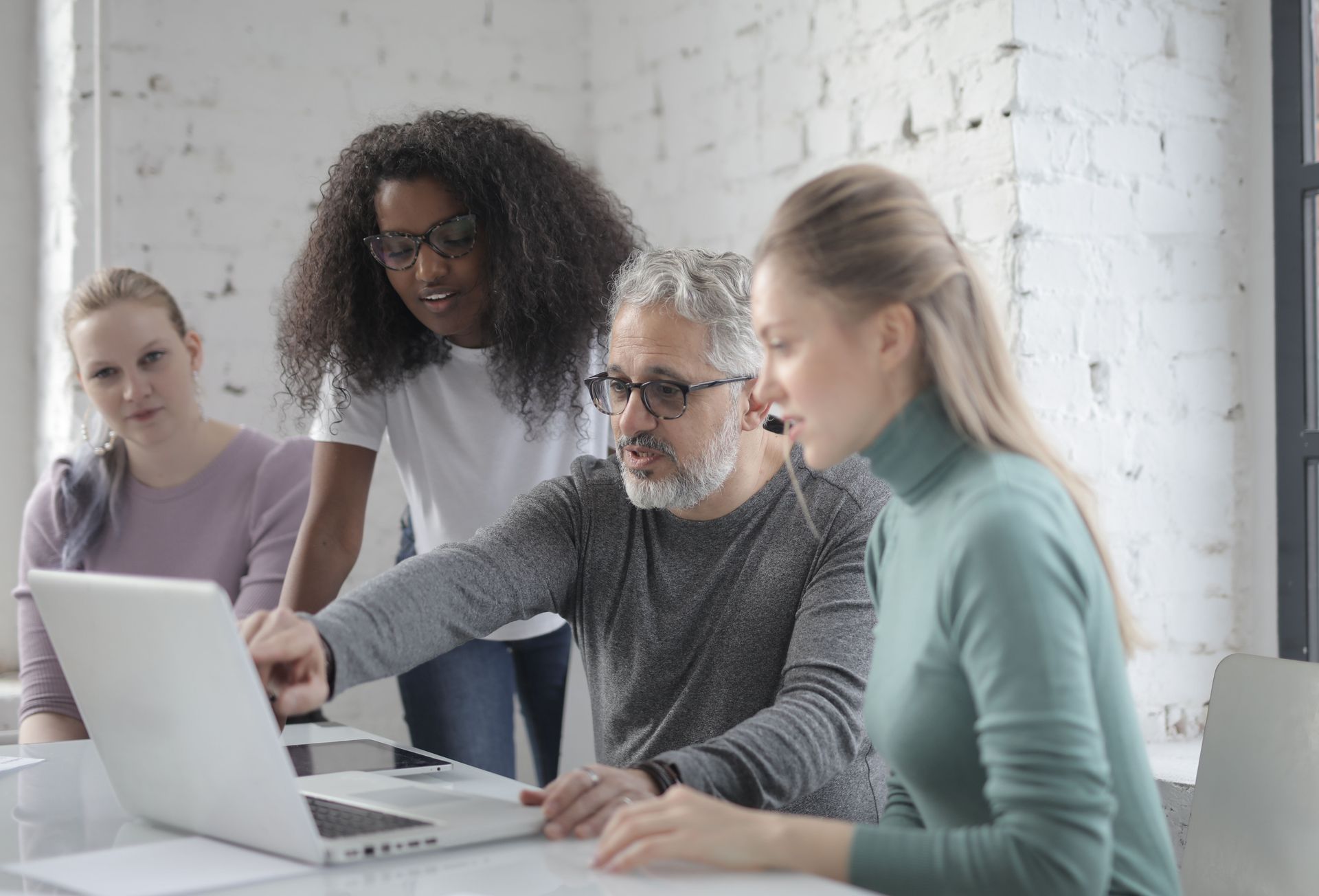 Four coworkers gathered around a laptop in a bright office, discussing work together.