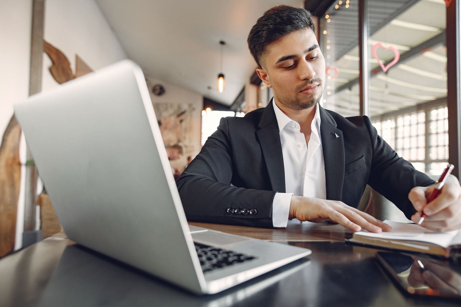 Man working at a laptop and taking notes at a desk in a bright office