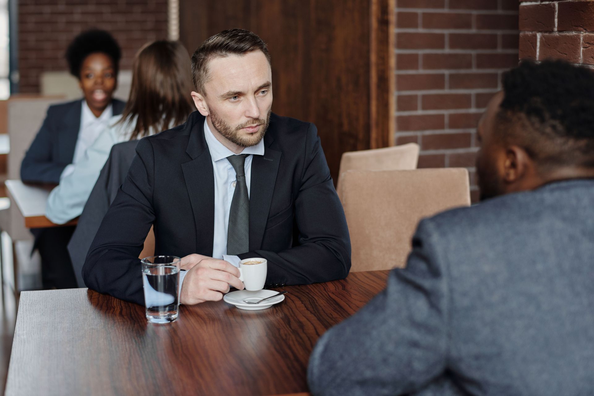 Two people in suits talking across a table during a business meeting