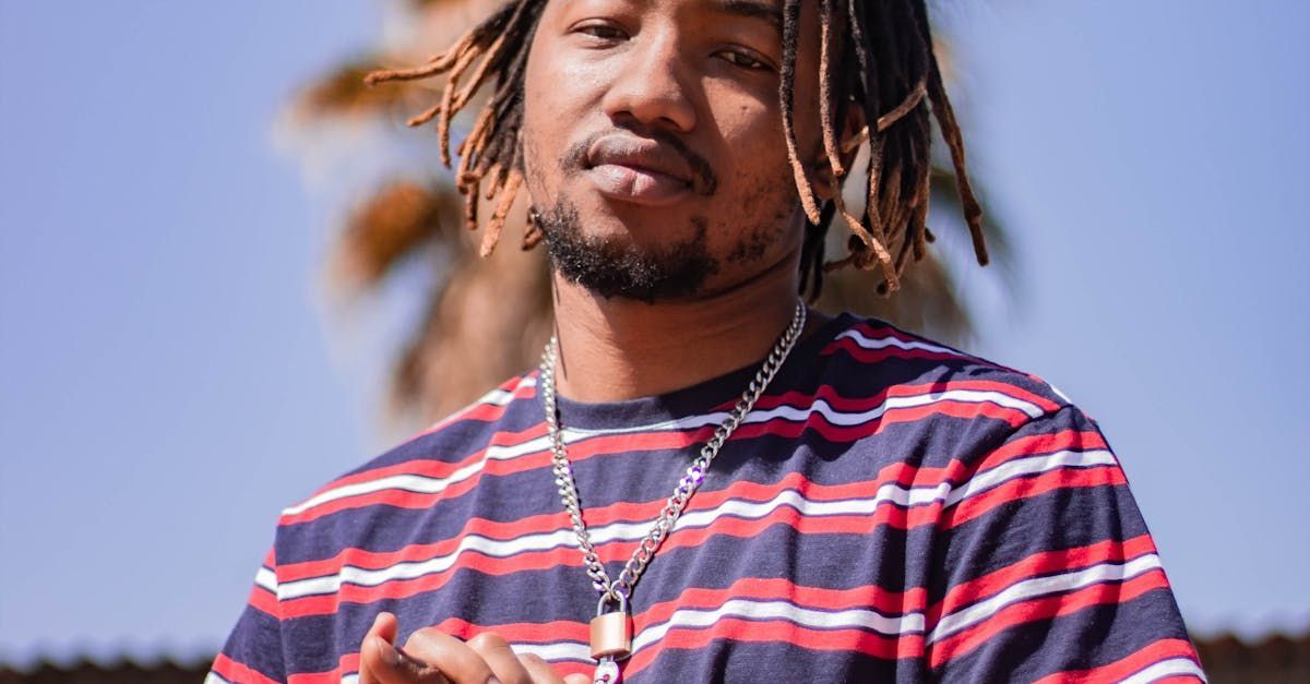 A man with dreadlocks is wearing a striped shirt and a necklace.