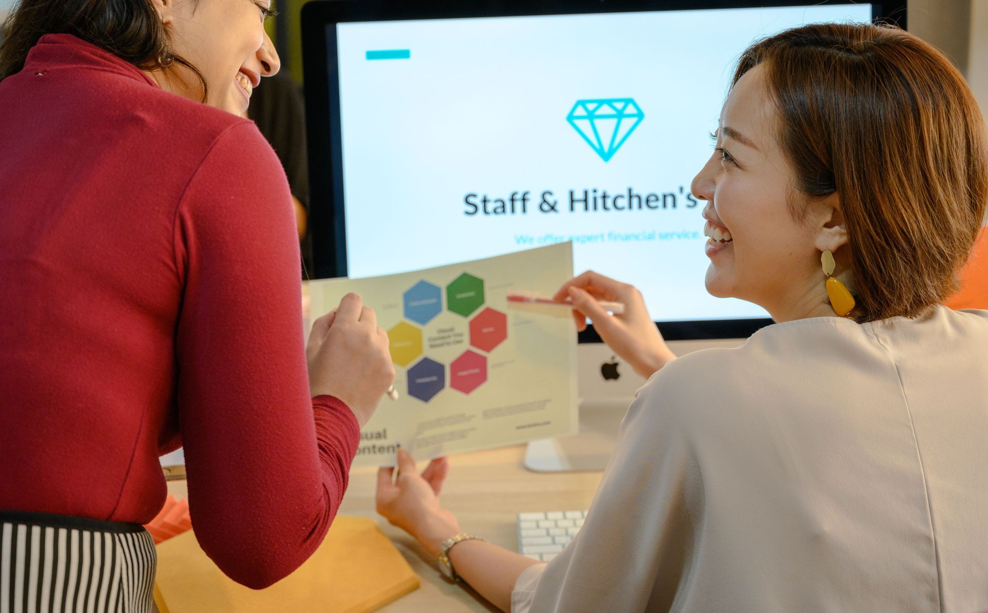 Two people collaborating at a monitor with sticky notes in an office setting
