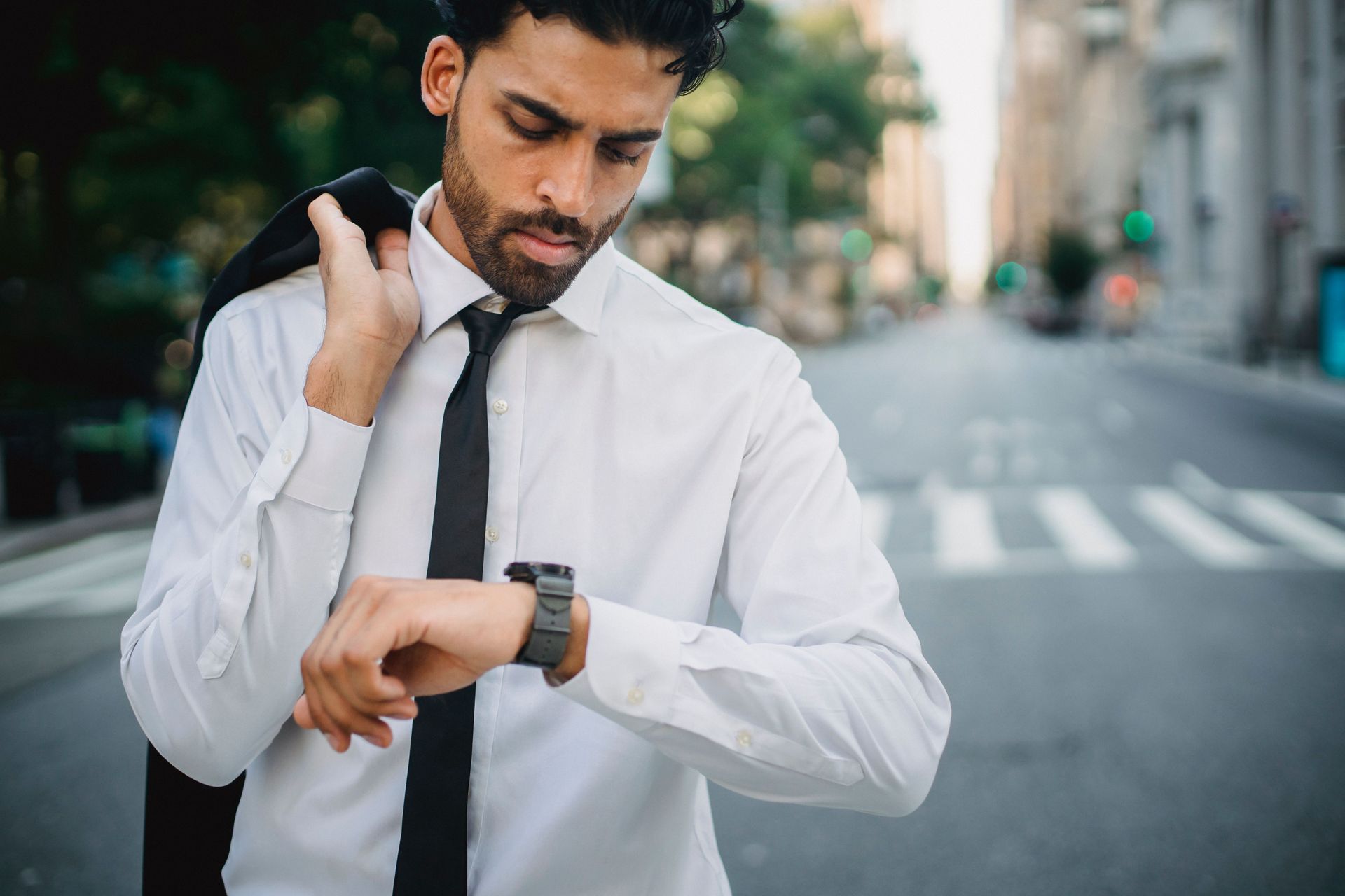 Man checking his wristwatch on a city street, wearing a white shirt and black tie.