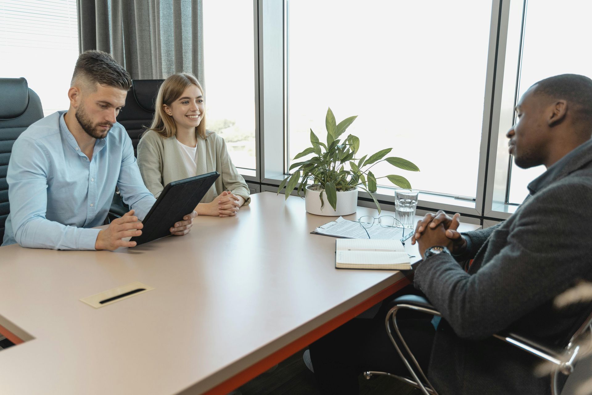 Three professionals sit at a light-colored desk in a modern office, engaged in a collaborative meeting.