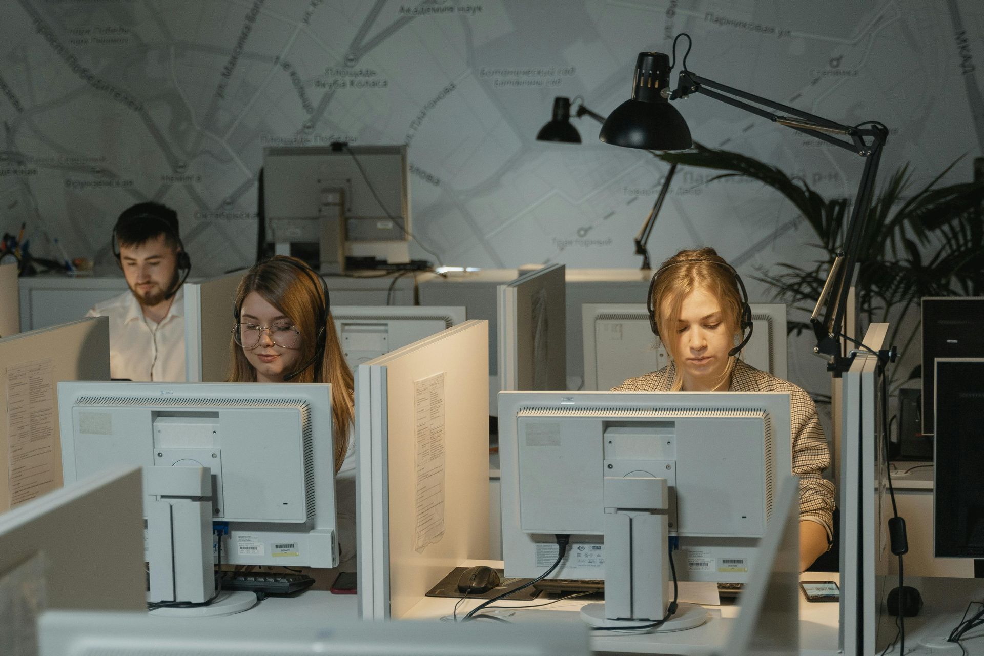 People working in a dimly lit office at computers, each wearing a headset.