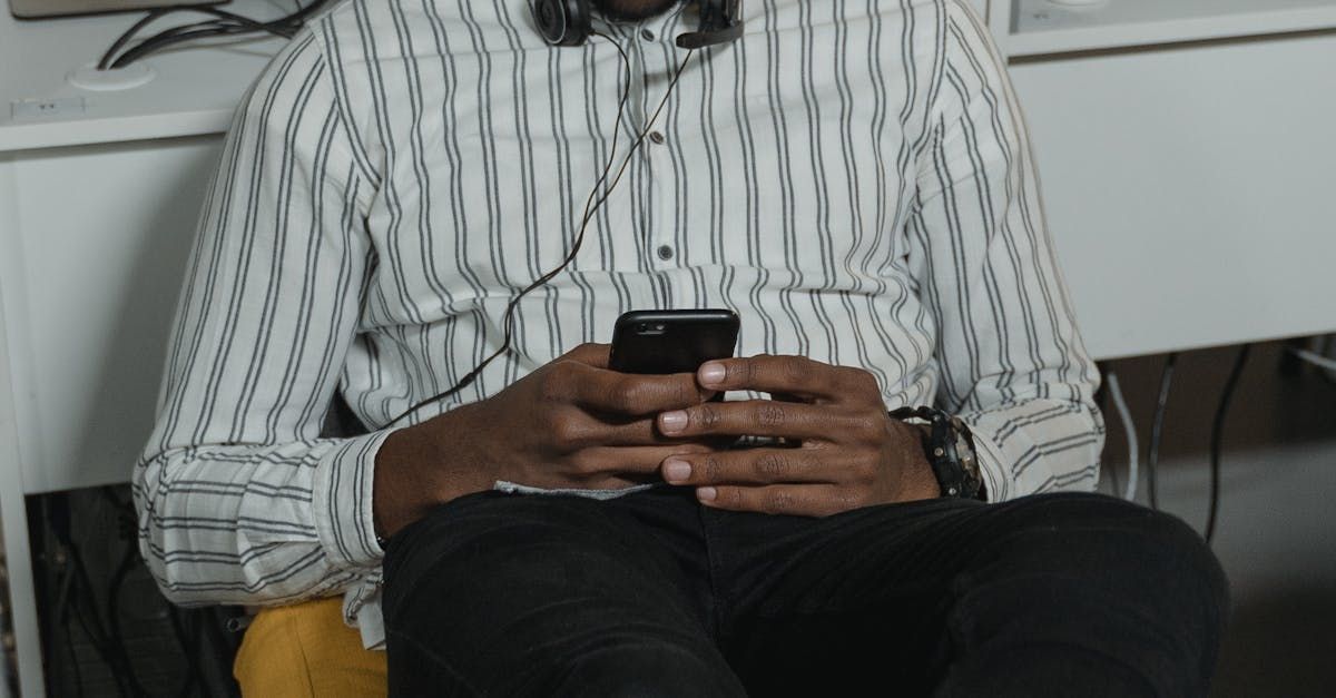 A man wearing headphones is sitting in a chair using a cell phone.