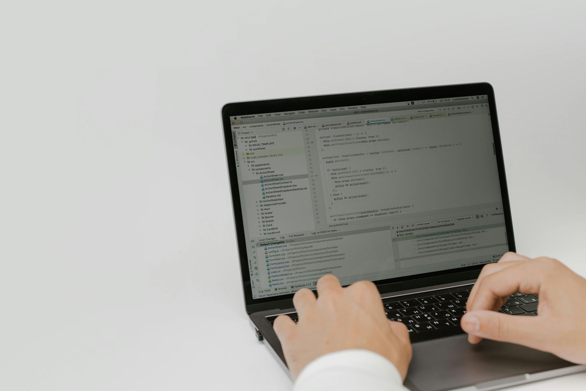 Hands typing on a laptop computer displaying code on its screen against a plain white background.
