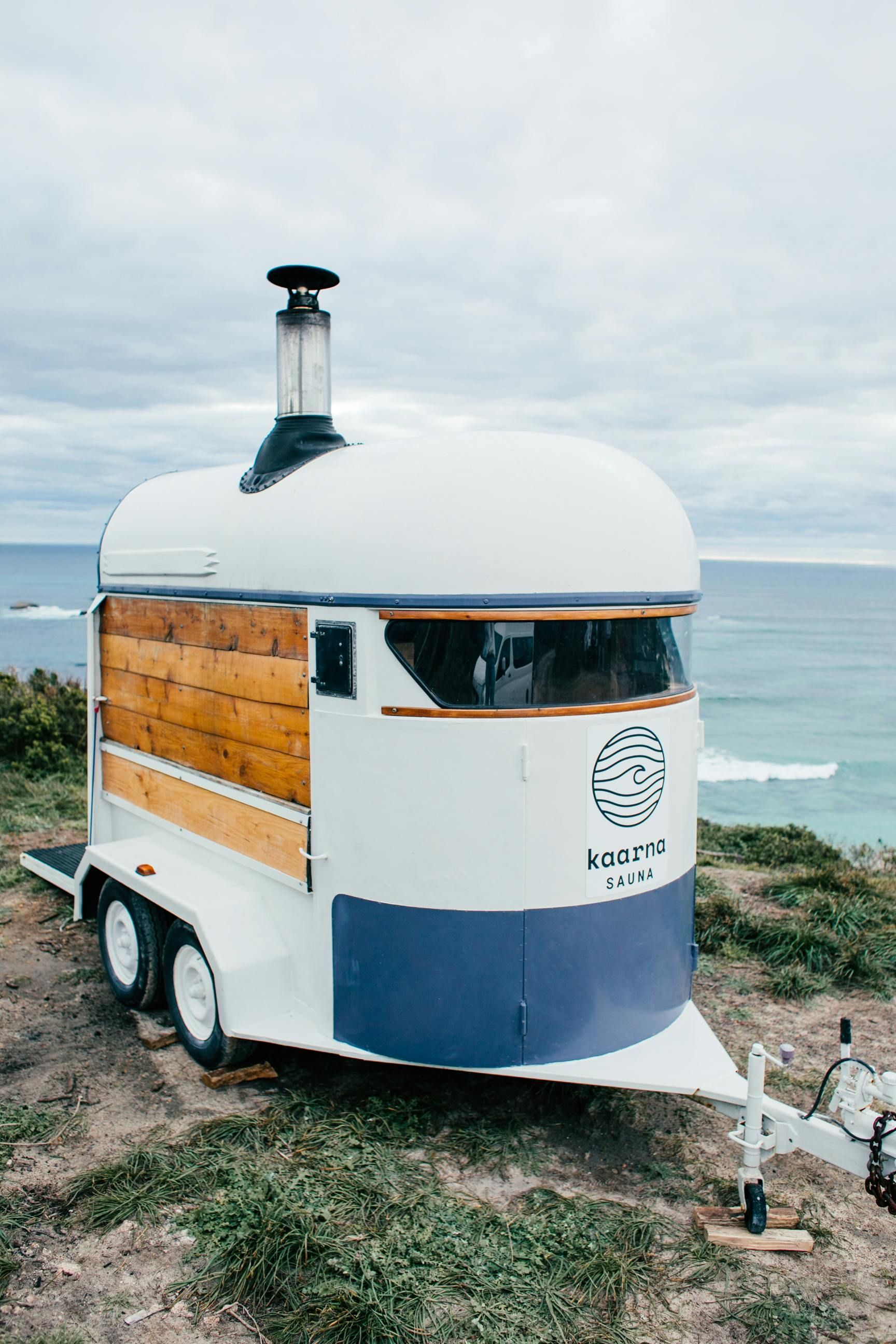 A trailer with a chimney on top of it is parked on a grassy hill near the ocean.