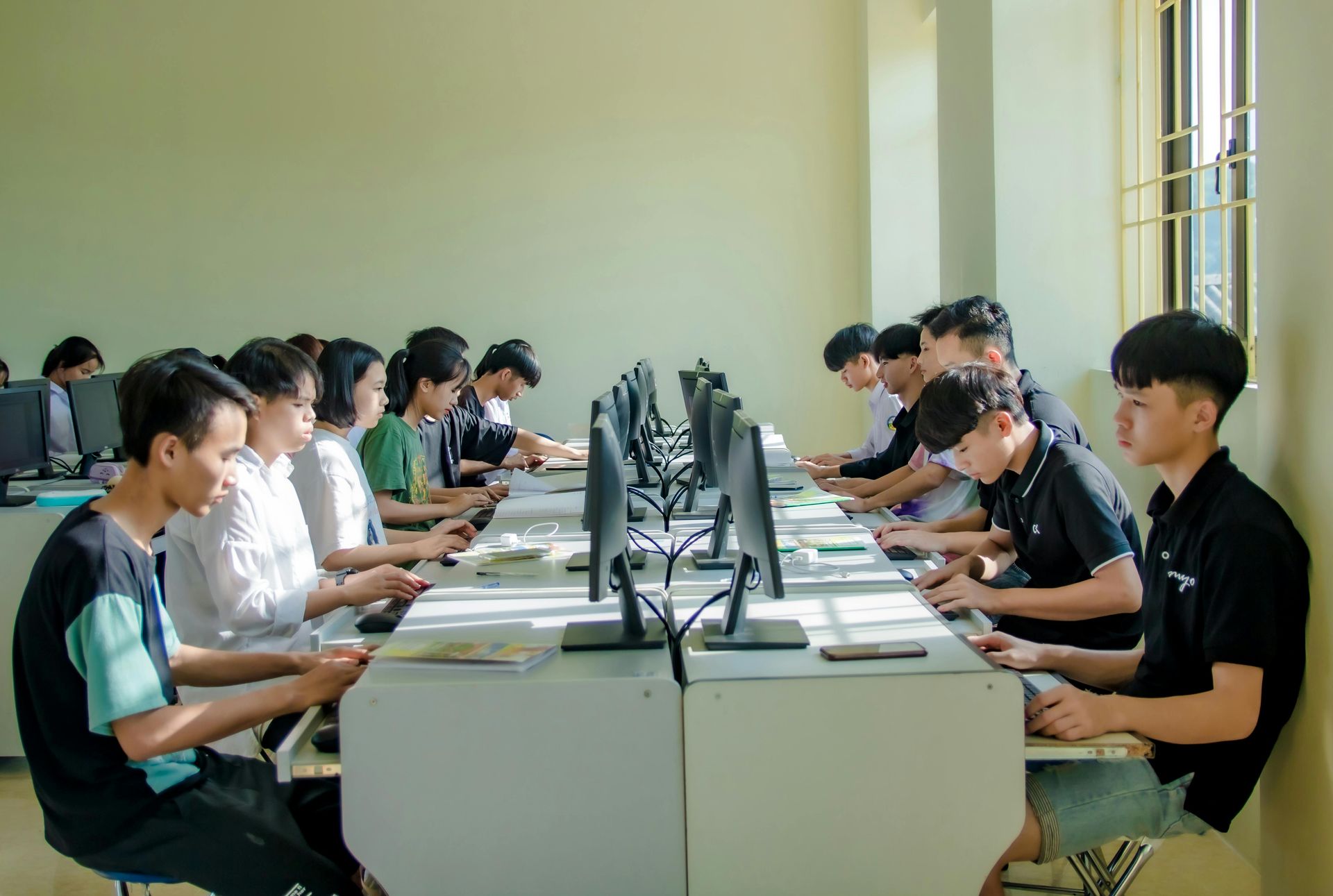 People seated at desktop computers in a bright computer lab, working side by side.