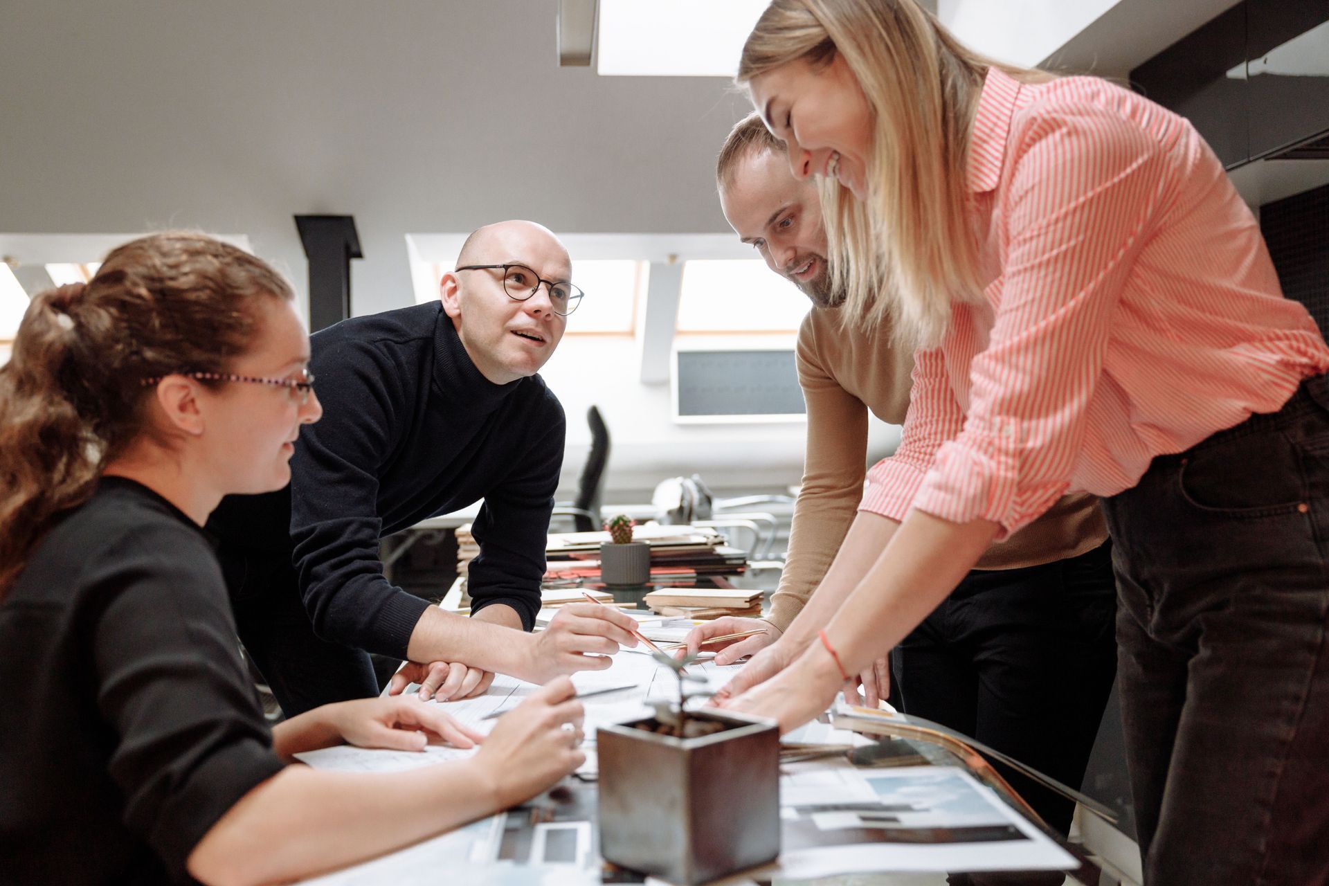 People gathered around a table in a bright office, discussing papers and leaning in together.
